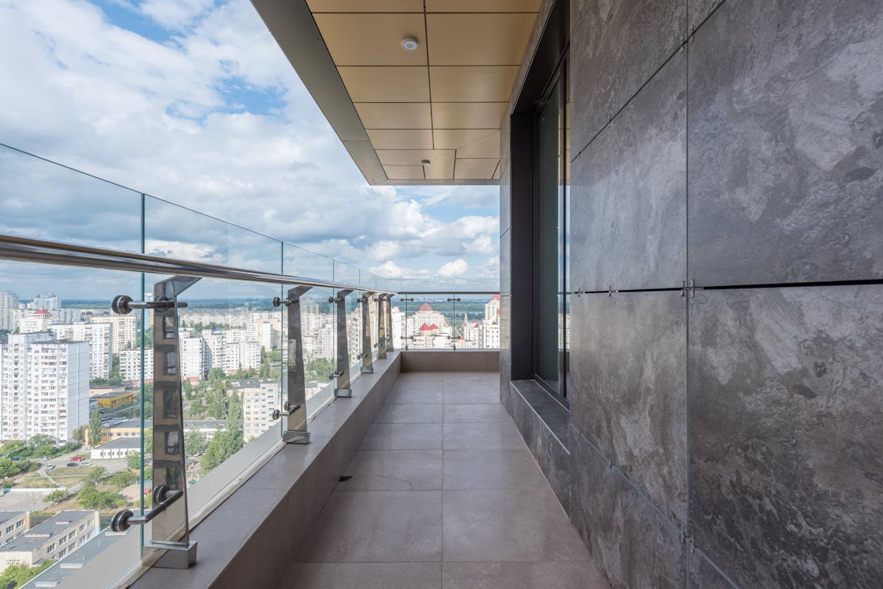 gallery-6 Spacious terrace with glass barrier and metal railings of contemporary apartment in multistory building against cloudy blue sky in city